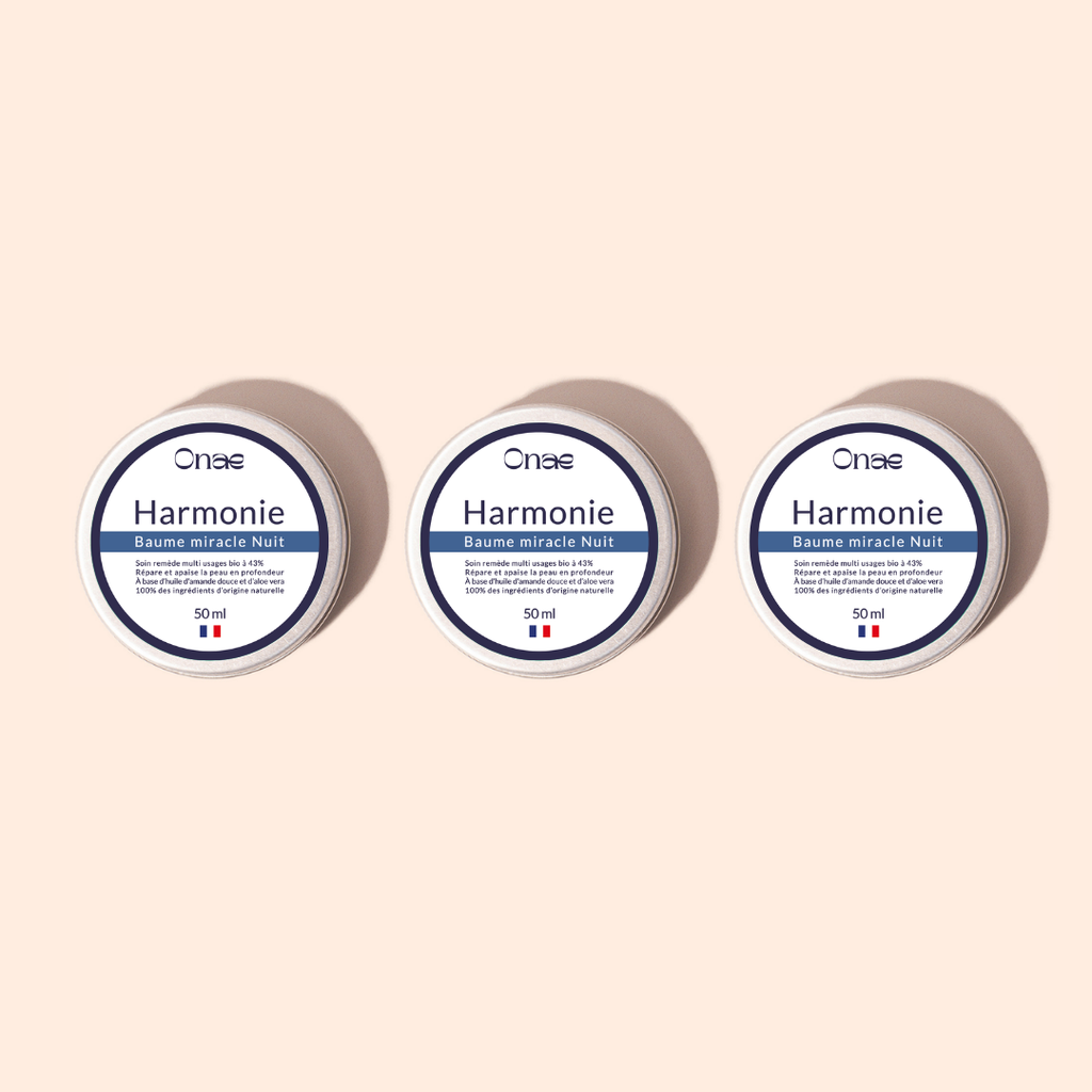 Trois pots identiques de baume de nuit réparateur avec étiquette blanche et bleue, posés sur un fond beige clair, évoquant un soin concentré en actifs végétaux pour la régénération de la peau.