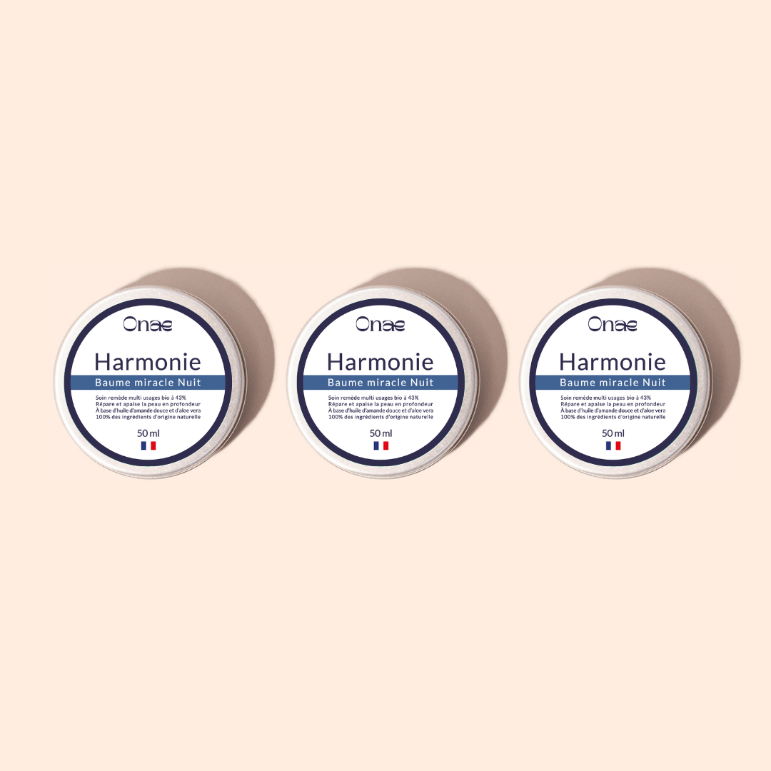 Trois pots identiques de baume de nuit réparateur avec étiquette blanche et bleue, posés sur un fond beige clair, évoquant un soin concentré en actifs végétaux pour la régénération de la peau.